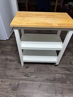 Front view showing butcher block top, white frame, two shelves, casters