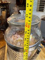 Full view of glass dispenser with measuring tape showing height ~17 inches