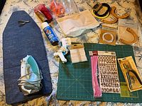 Full lot overview showing ironing board, iron, cutting mat, glue gun, spray paint, ribbons, handles, zipper, stickers