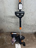 Full view of WORX string trimmer standing upright with charger, batteries, spool pack and manual at base