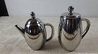 Two stainless steel items, coffee press right, teapot left