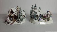 Both Thomas Kinkade Christmas village sculptures side by side