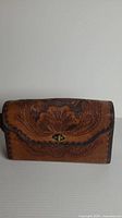 Front view of hand-tooled leather purse showing floral design, braided edges, brass turn-lock