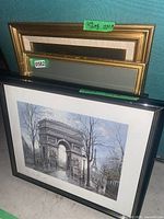 Stack of framed artworks showing black Paris print and additional frames behind