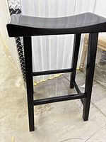 Side view of one stool showing saddle seat, legs, and stretcher