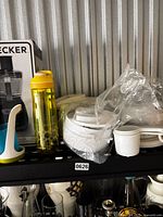 Shelf view showing boxed Black+Decker food processor, yellow bottle, white plastic bowls, measuring cups, biscuit extruder