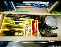 Drawer overview showing assorted utensils, cutlery tray, mesh strainer, can openers, measuring spoons, silicone spoon, whisk