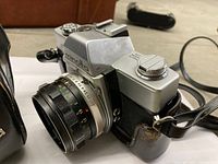 Left front view of camera with lens attached, leather case partially visible