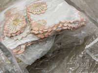Multiple hand-embroidered linens with pink and gold scalloped floral edges in plastic bag