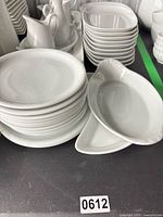 Stacks of white round plates, oval serving dish, pitchers visible