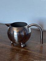 Side view of spherical stainless steel creamer showing handle and spout