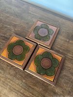 Three framed ceramic tiles arranged on tabletop showing design