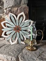 Chamberstick with glass shade and flower wall sculpture on stone hearth