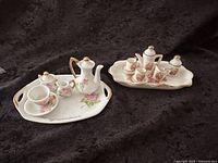 Both complete miniature tea sets displayed on dark fabric