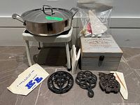 Group shot showing sauté pan, step stool, three cast iron trivets, pastry bags, wooden box