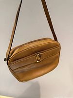 Full view of front of tan leather Ferragamo shoulder bag hanging by strap