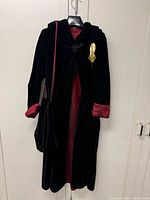 Coat displayed on hanger showing full length, red lining, bag hanging and gold-tone buckle attached