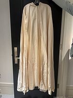 Front view of full-length cream satin cloak hanging, shows overall length and sheen