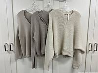 Front view of all three sweaters hung side by side