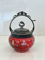 Front view showing cranberry glass body, enamel flowers, silver-plated lid and handle