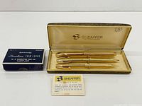 Full set displayed: three gold writing instruments in Sheaffer case, leads box and leaflet