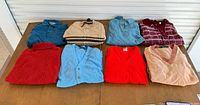 Eight folded vintage men’s sweaters on table