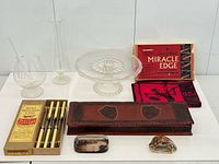 Group shot of all items including boxed cutlery, glass pieces, tea towel, cake stand, dish and seashell