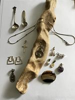 Full lot overview with spoons, necklaces, earrings, pendants and brooch on driftwood