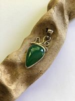 Front view of sterling silver pendant on wood prop showing green teardrop cabochon and scroll top