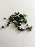Group of various size dark green jade beads scattered on white background