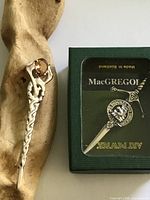 Both kilt pins shown; boxed Art Pewter pin at right, unboxed twisted thistle pin at left