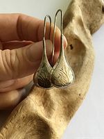 Pair of sterling silver etched teardrop earrings held to show front detail