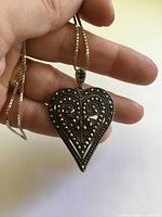 Close-up of heart pendant held in hand showing marcasite detail and scale