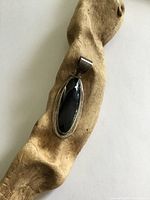 Front view of sterling silver pendant resting on driftwood