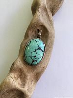 Front view of pendant on driftwood showing turquoise cabochon