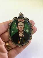 Front view of pendant in hand showing portrait and scalloped silver frame