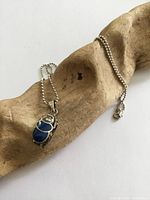 Necklace laid on driftwood showing full chain, pendant, and clasp