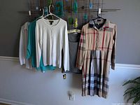 Group view of four garments on hangers: white shirt, green blouse partially visible, gray tank, beige plaid dress