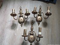 Three brass two-light wall sconces on floor