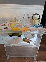 Overall lot on acrylic shelf showing saucers, cups, bowls, dispensers, clowns, casserole, plate, planter, spoon, tongs, candle holders
