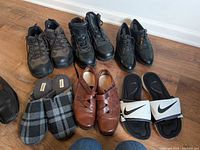 All six pairs laid out: two pairs of work boots, black wingtip dress shoes, brown leather shoes, plaid slippers, Nike slide sandals