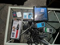 All items on glass table: boxed HP stand, sealed engraver, outlet timer, pin tin, two cable testers with cables