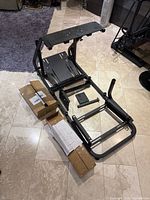 Overhead view of partially assembled black metal racing simulator stand with mounting plates and three cardboard boxes