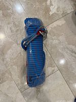 Coiled blue heavy duty rope in plastic wrap with metal shackle and red sleeve visible