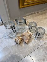 Three Le Parfait glass clamp jars and two conch shells on marble floor