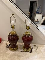 Pair of burgundy ceramic table lamps with brass bases, handles, harps and finials, cords visible