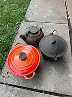Three cast iron pieces: orange Le Creuset Dutch oven, dark kettle, hammered pot with lid