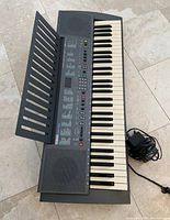 Top view of Yamaha PSR-300 keyboard with music rest attached and power cable beside