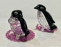Front view of two Swarovski crystal penguin figurines on purple bases