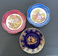 Top view showing three colored Limoges dishes with gilt borders and scenes